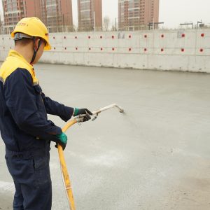 Professional applying waterproofing coating to concrete foundation surface